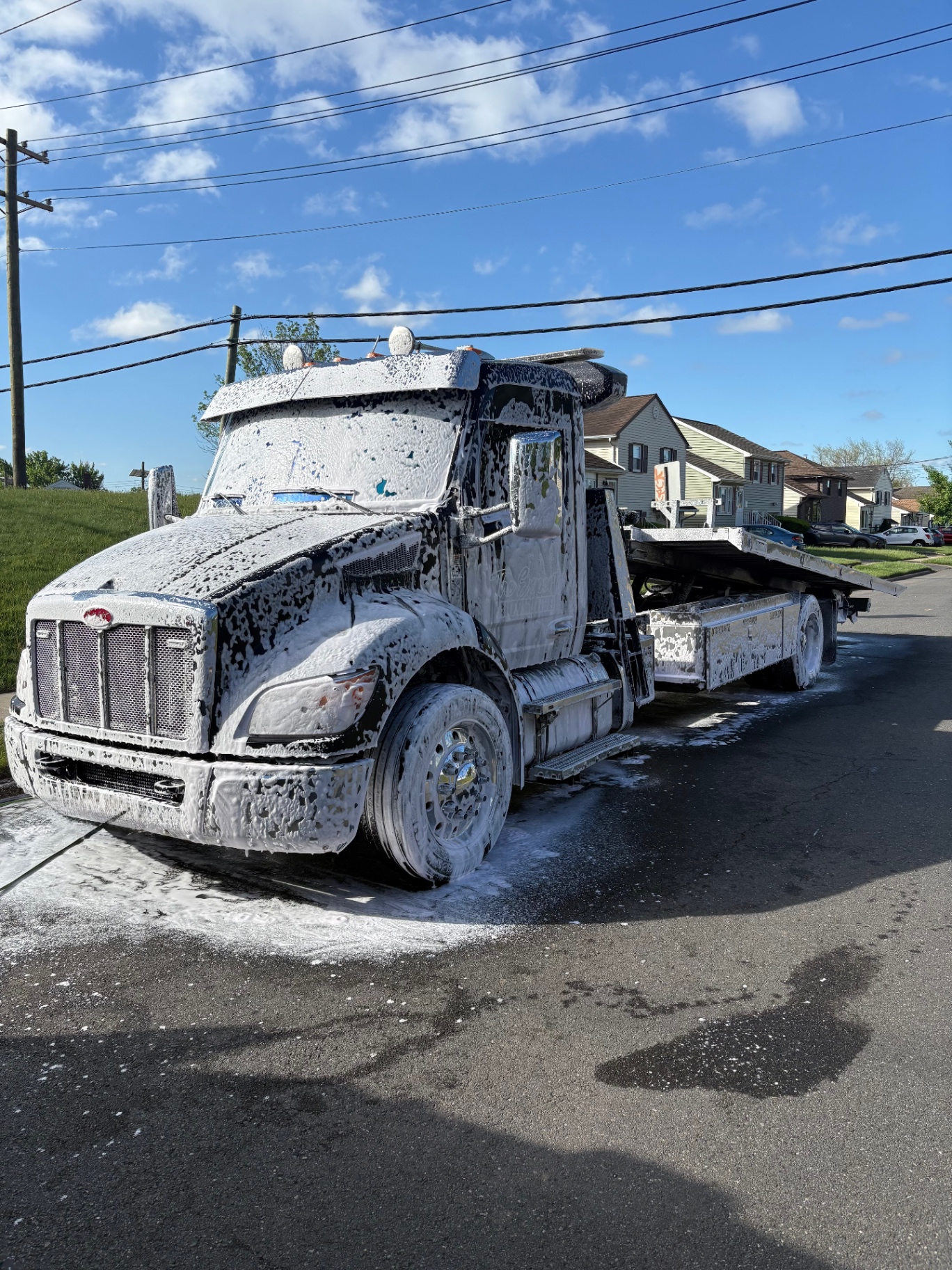 Black Peterbilt flatbed tow truck blanketed in thick snow foam during heavy-duty pre-wash