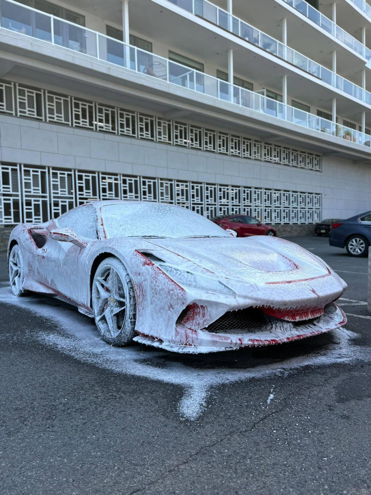 Red Ferrari F8 Tributo blanketed in thick snow foam during decontamination wash