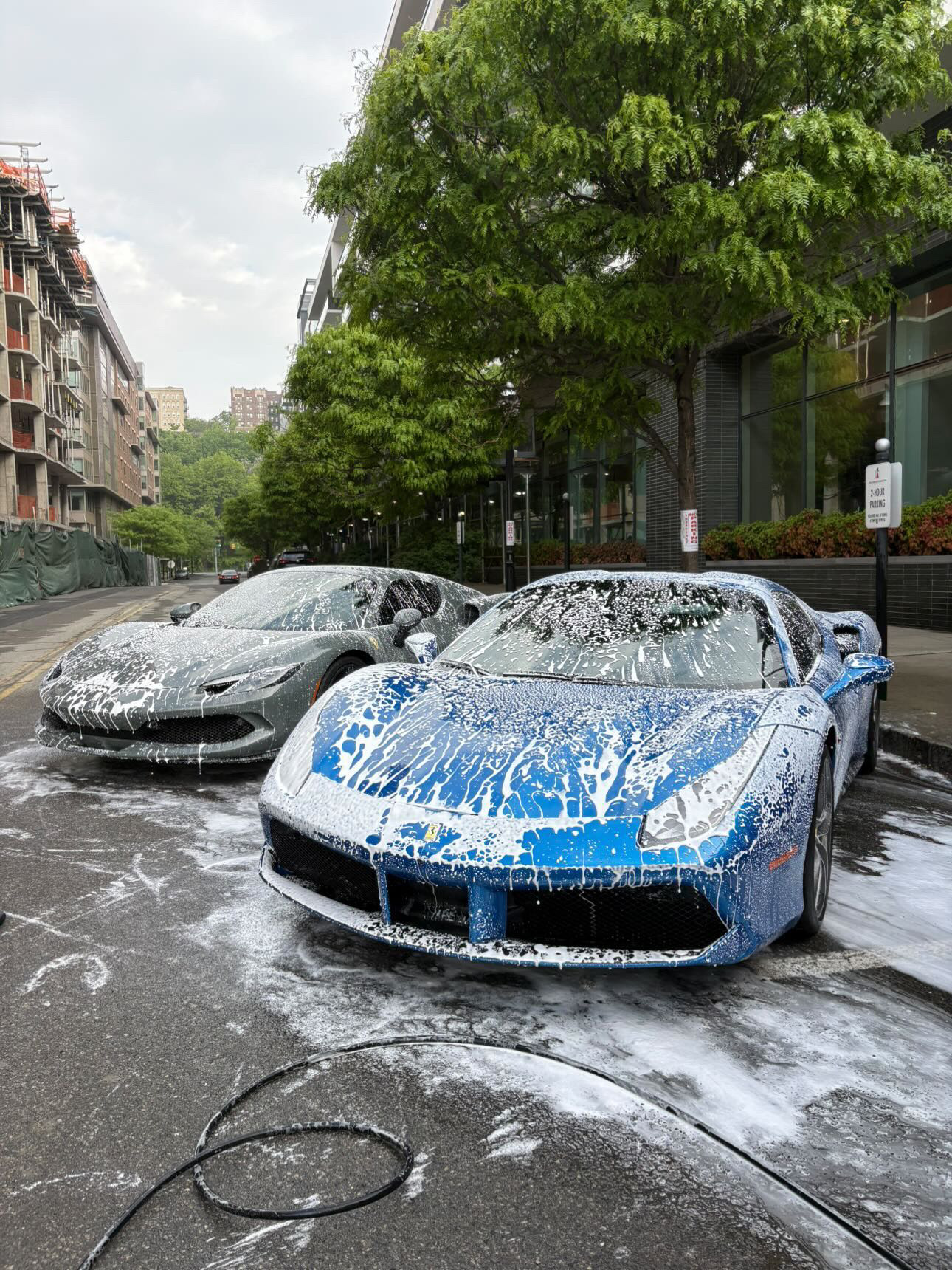 Two Ferraris — a grey 296 and a blue 488 — covered in snow foam during a Family Fleet Club mobile detail visit
